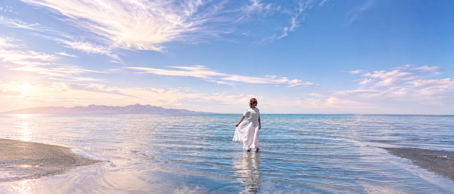 澄んだ海辺の浅瀬に、白い服で立つ人